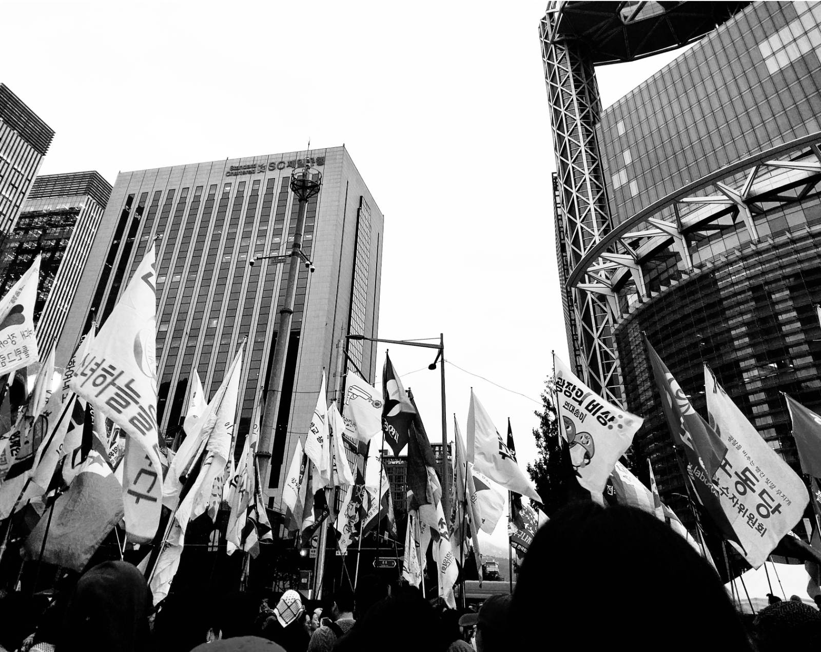 [그림 5: 흑백의 사진 속에는 한 무리의 군중이 깃발들을 세우고 고층 빌딩들 앞의 광장에 모여있다.]